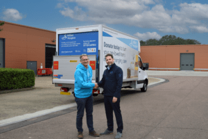 Team members from willen hospice shaking hands in front of liveried van.